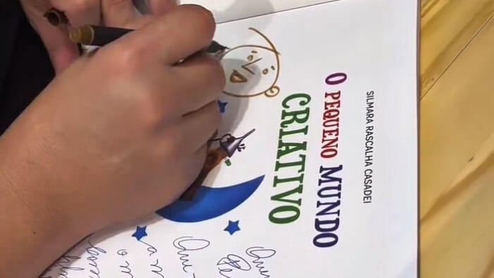 Detalhe de mãos do ilustrador Ricardo Girotto fazendo um desenho personalizado na dedicatória do livro infantil O Pequeno Mundo Criativo.