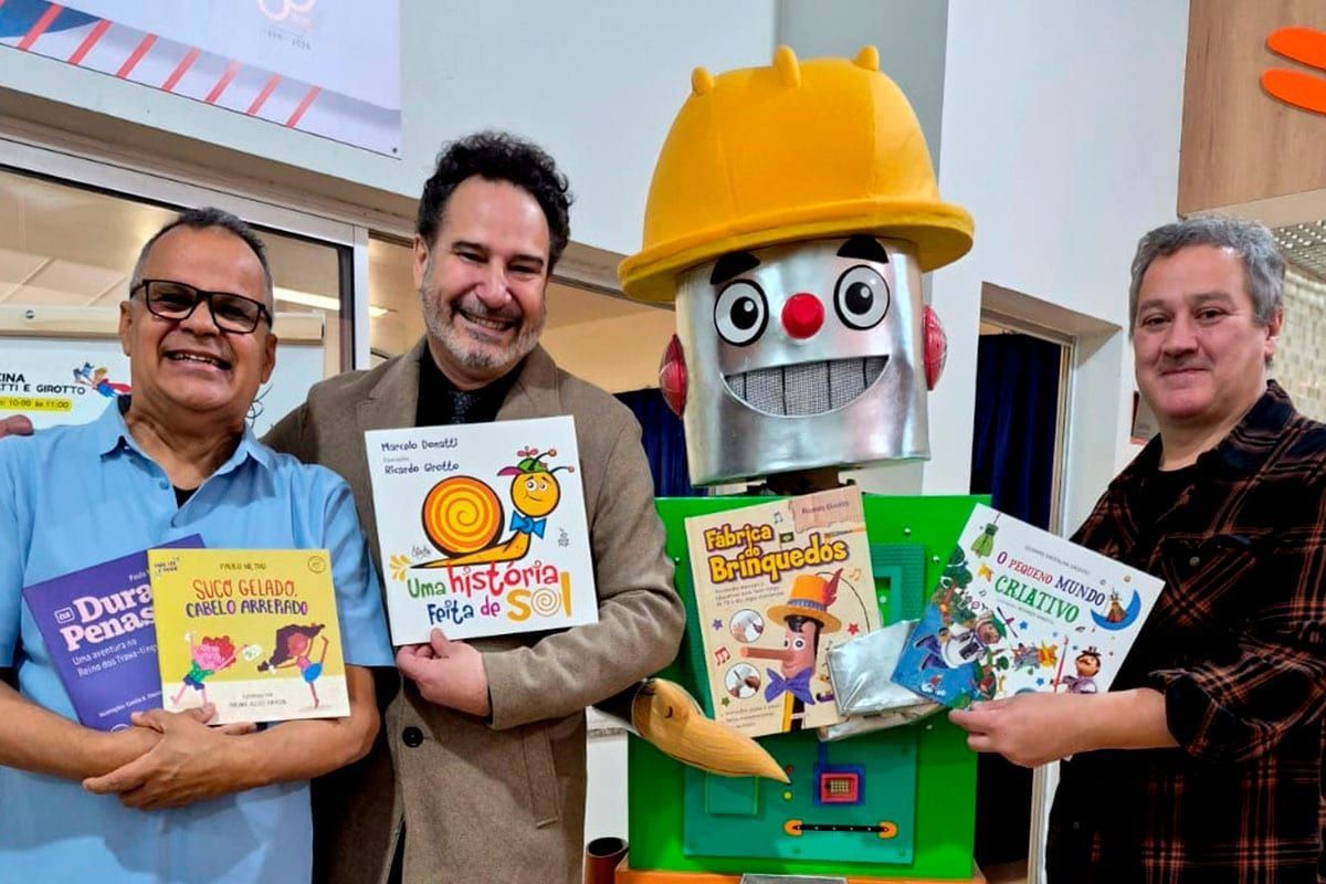 Ricardo, Marcelo e Paulo interagindo com o público ou ao lado da exposição de livros.